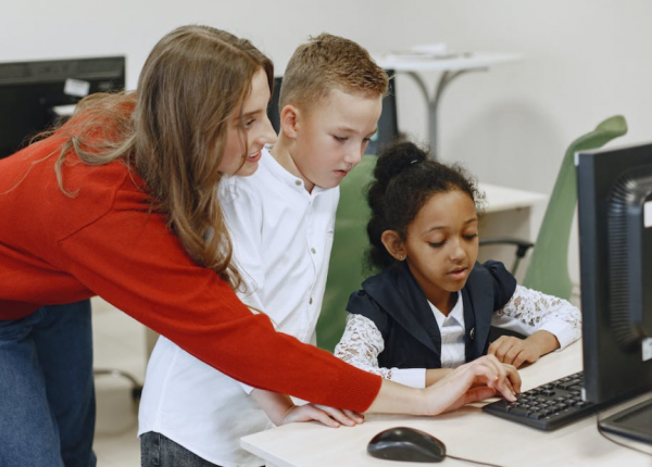 Two kids on computer with teacher